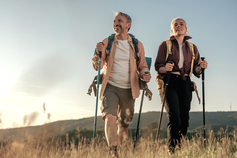 Middle age couple hiking and following trail along grassy mountain ridge