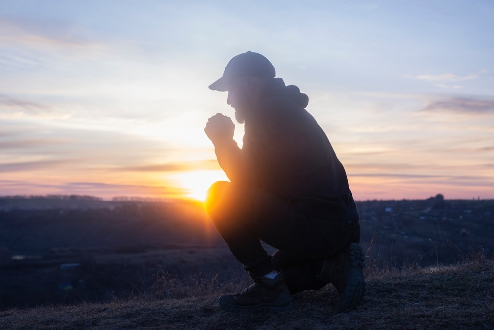 A man on his knees praying on the background of the sunset sky